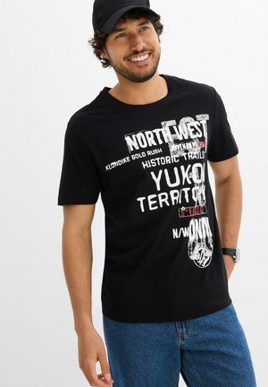 T-shirt nera in cotone con grafica audace in bianco e rosso, maniche corte e scollatura rotonda, abbinata a jeans blu.