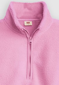 Pull polaire rose clair avec col montant et fermeture éclair à moitié ; surface texturée avec une apparence douce et confortable.