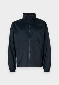 Jachetă din material ușor de culoare bleumarin, tip windbreaker, cu guler înalt, fermoar complet pe față și manșete elastice pentru o potrivire sigură.