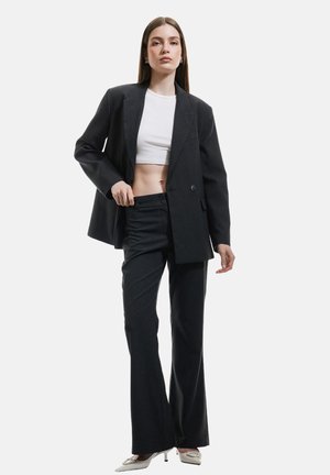 Blazer noir ajusté avec revers en pointe sur un top court blanc, associé à un pantalon sombre et des chaussures à talons hauts argentées.