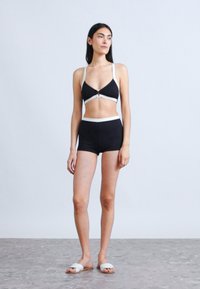 Svart bikini med hvite detaljer, bestående av en trekantet bh og høytlivsshorts. Glatt stoff, minimalistisk design.