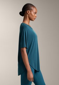 Zöldeskék, laza szabású póló rövid ujjakkal és ívelt szegéllyel. Sima textúra, laza stílus, összehangolt leggingsszel párosítva.