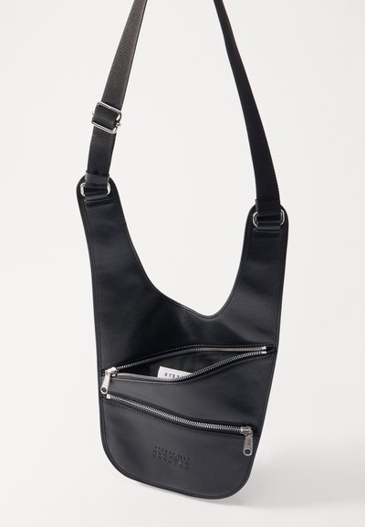 Borsa a spalla in pelle nera con design curvo, dotata di due tasche con cerniera, hardware in argento e una tracolla in tessuto. Texture liscia.