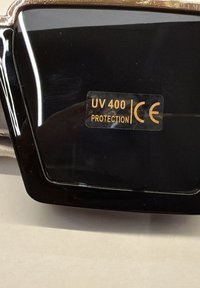 Schwarze Sonnenbrillengläser mit einem goldenen Aufkleber "UV 400 Protection" und CE-Kennzeichnung auf der Oberfläche.