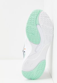 Semelle de chaussure de sport blanche avec bande de roulement en caoutchouc vert clair, texturée pour l'adhérence, positionnée sur un fond blanc en angle.
