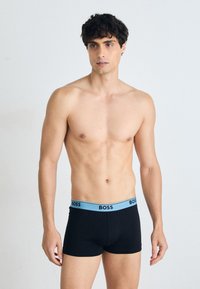Schwarze Boxershorts mit hellblauem Bund, der das "BOSS"-Logo zeigt. Der Stoff wirkt glatt und dehnbar und bietet eine eng anliegende Silhouette.