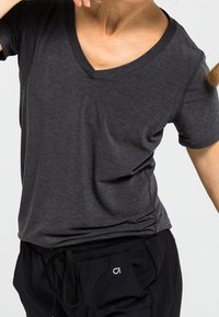 T-shirt gris foncé à manches courtes et col en V, fabriqué en matière douce, associé à un pantalon noir à cordon de serrage, présentant un design simple et une coupe décontractée.