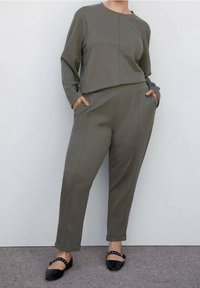 Olivenfarbenes Loungewear-Set aus weichem Stoff; besteht aus einem Langarmoberteil mit Rundhalsausschnitt und passenden, taillierten Hosen mit Taschen.