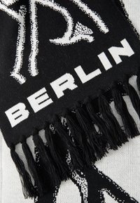 Black and white scarf with fringe detailing; features text "BERLIN" and a graphic design, woven texture, and a bold pattern.