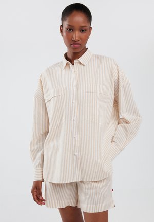 Beige og hvid stribet skjorte med knapåbning og to brystlommer, parret med matchende shorts. Lavet af letvægtsstof med en afslappet pasform.