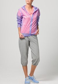 Giacca zip-up trasparente viola e rosa con pois sopra una maglietta rosa, abbinata a pantaloni sweat cropped grigi e sneakers azzurro chiaro.