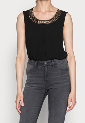 Top nero senza maniche con scollatura rotonda e decorazioni di bronzo e nero scintillanti; abbinato a jeans grigi aderenti.