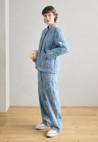Giacca trapuntata azzurra chiara con un motivo testurizzato, abbinata a pantaloni a gamba larga coordinati, completata da sneaker bianche.