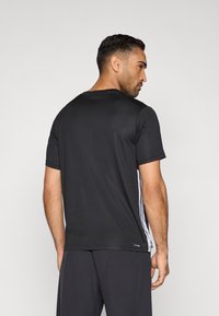 Camiseta deportiva negra de manga corta, con cuello redondo y textura sutil. Presenta rayas blancas a lo largo de los costados para contraste.