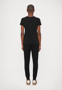 Tricou din bumbac negru cu mâneci scurte, asortat cu pantaloni de trening negri și adidași cu un design verde și alb.