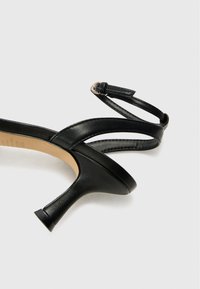 Sandale à talons hauts en cuir noir avec une fine bride au niveau de la cheville, un bout pointu et une tige texturée, dotée d'un design de talon profilé.