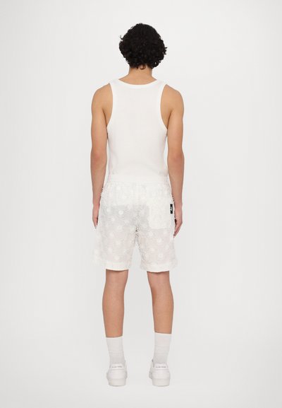 Hvid tanktop og mønstrede hvide shorts med broderede solformer. Shorts har en elastisk talje og en sidelomme. Hvide sneakers.