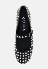 Black Mary Jane flat shoe with silver studs and buckle strap, displaying "GUESS" logo on the insole.