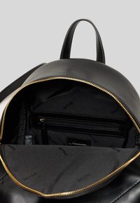 Zaino in pelle nera con zip dorata, fodera in tessuto, tasca interna con zip e motivo logo sulla fodera. Due manici superiori sono visibili.