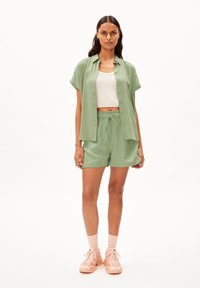 Lichtgroen kortarm overhemd met knopen en bijpassende shorts, laag over een witte geribbelde crop top. Sneakers zijn roze met gestructureerde accenten.