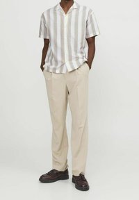 Korte mouwen gestreept shirt in wit en pastelkleuren, met een notch-kraag, gecombineerd met beige broeken en schoenen met donkere bruine franjes.