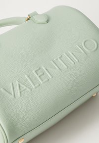 Svetlozelena usnjena torbica z teksturirano površino, vtisnjenim logotipom "VALENTINO" in zlatimi kovinskimi dodatki. Okrogla oblika.