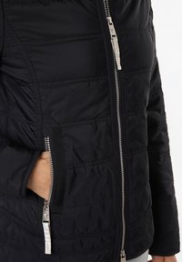 Marineblaue gesteppte Jacke mit silbernem Reißverschluss, seitlichen Taschen und elastischen Details. Sie zeichnet sich durch eine leichte, gepolsterte Textur aus, die Wärme bietet.