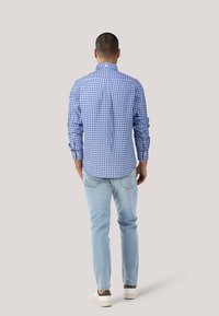 Blau-weißer karierten Hemd mit langen Ärmeln, Knopfkragen und Falten-Detail auf der Rückseite, kombiniert mit hellblauen Jeans und weißen Sneakers.
