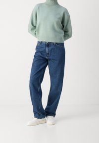 Mint green, knitted sweater with high neckline; blue, loose-fitting denim jeans; white sneakers complete the casual outfit.