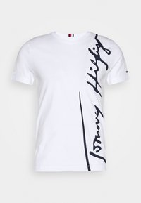 Camiseta de algodón blanca con un gran logotipo en script negro en el lado izquierdo. Diseño de mangas cortas y cuello redondo. Detalle de rayas horizontales en el cuello.