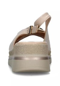 Sandal in un beige chiaro con una suola texturizzata, cinturino alla caviglia regolabile e un tacco leggero. Presenta un materiale superiore morbido e dettagli in metallo dorato.