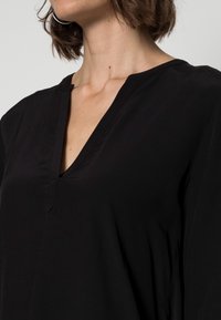 Top nero a V in morbido tessuto, con una vestibilità comoda e un design minimale, arricchito da un dettaglio a chiave all'scollatura.