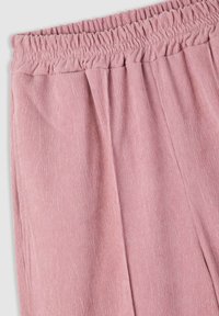 Pantaloni di velluto a coste in morbido rosa, con una cintura elastica, texture a coste verticali e leggere pieghe sul davanti.
