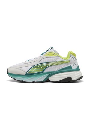 Chaussure de sport blanche avec des accents verts et jaunes, une semelle verte épaisse et une semelle extérieure noire arrondie, vue de profil latéral.