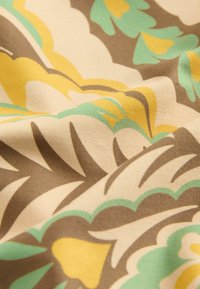 Kwiatowy materiał w kolorze kremowym, z dużymi żółtymi, zielonymi i brązowymi wzorami. Tekstura jest gładka z delikatnym połyskiem.