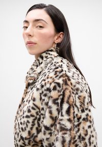 Umelá kožušina s leopardím motívom, s vysokým golierom a mäkkou textúrou. Farebná paleta obsahuje béžové, hnedé a čierne vzory.