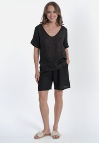 Top corto a maniche corte in lino nero con scollatura a V e pantaloni coordinati. Il tessuto è leggero, con una vestibilità ampia e una sottile texture. Sandali a infradito bianchi.