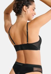 Ensemble de lingerie noire comprenant un soutien-gorge en dentelle transparente avec des straps réglables et un bas taille haute assorti, mettant en valeur des textures lisses et un design courbé.