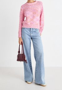 Růžový a oranžový melírovaný pletený svetr, široké modré džíny a malá bordó kabelka s dvěma uchy. Ležérní outfit s texturovaným povrchem.