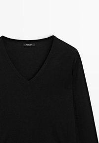 Pull noir à manches longues avec col en V et étiquette de marque visible à l’intérieur du col sur fond blanc.