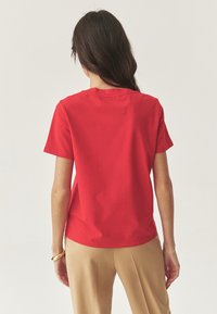 Rød bomulds T-shirt med korte ærmer og rund halsudskæring, der har en glat tekstur og en afslappet pasform. Bagfra er der rene linjer.
