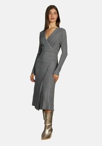 Rochie gri cu dungi, cu mâneci lungi, decolteu în V adânc și design înfășurat. Prezintă o fustă de lungime medie și este asortată cu botine metalice până la gleznă.