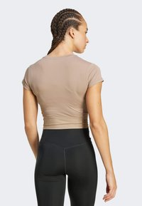 Top corto ajustado de color marrón claro con mangas cortas y dobladillo acanalado, combinado con leggings negros de cintura alta. Textura suave.
