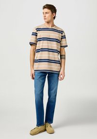 Camiseta a rayas beige con líneas horizontales en azul marino y blanco, combinada con jeans azules y zapatos tipo mocasín de color claro.