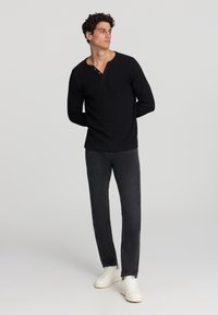 Maglietta henley nera a maniche lunghe con texture a coste, dotata di una placca con tre bottoni. Abbinerà a jeans scuri e sneakers bianche.
