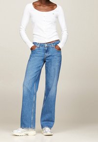 Camisa blanca de manga larga con escote en forma de bote, combinada con pantalones vaqueros azules de pierna ancha que cuentan con cinco bolsillos y un cierre de botón en el frente.