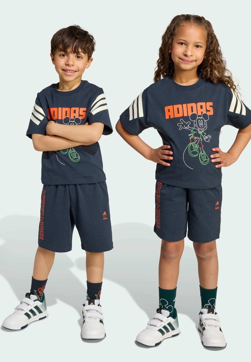 Completo sportivo per bambini di colore blu navy composto da una maglietta con il testo arancione "ADIDAS" e una grafica di Topolino, abbinato a pantaloni corti coordinati.