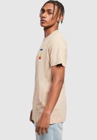 Beige cotton t-shirt with short sleeves, featuring a blue "SPORTS" text and a colorful graphic of a drink on the front.