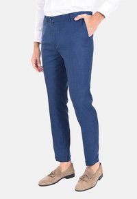 Pantaloni su misura blu con una texture liscia, un discreto motivo a quadri, vestibilità slim, tasche laterali e orlo con risvolto. Indossati con mocassini beige.