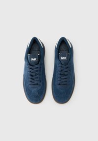 Μπλε σουέντ αθλητικά παπούτσια με στρογγυλεμένη μύτη, υφασμάτινο πάνω μέρος, επίπεδα κορδόνια και σκούρα λαστιχένια σόλα. Διαθέτουν ετικέτα με λογότυπο στη γλώσσα.